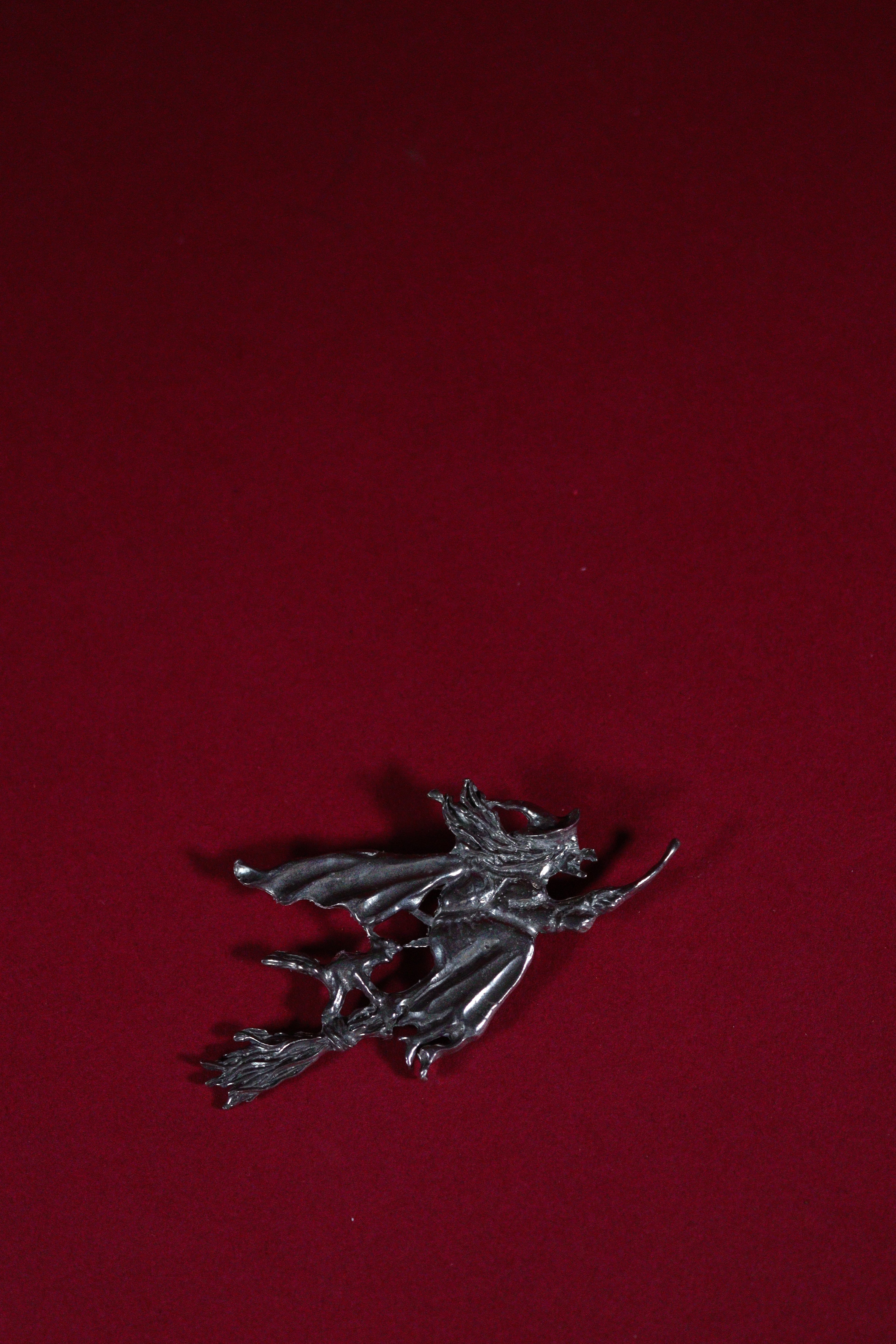 Metallic witch on a broom figurine on a red background
