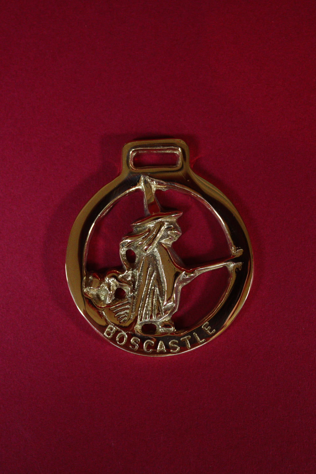 Brass pendant with a witch design on a red background