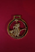 Brass pendant with a witch design on a red background