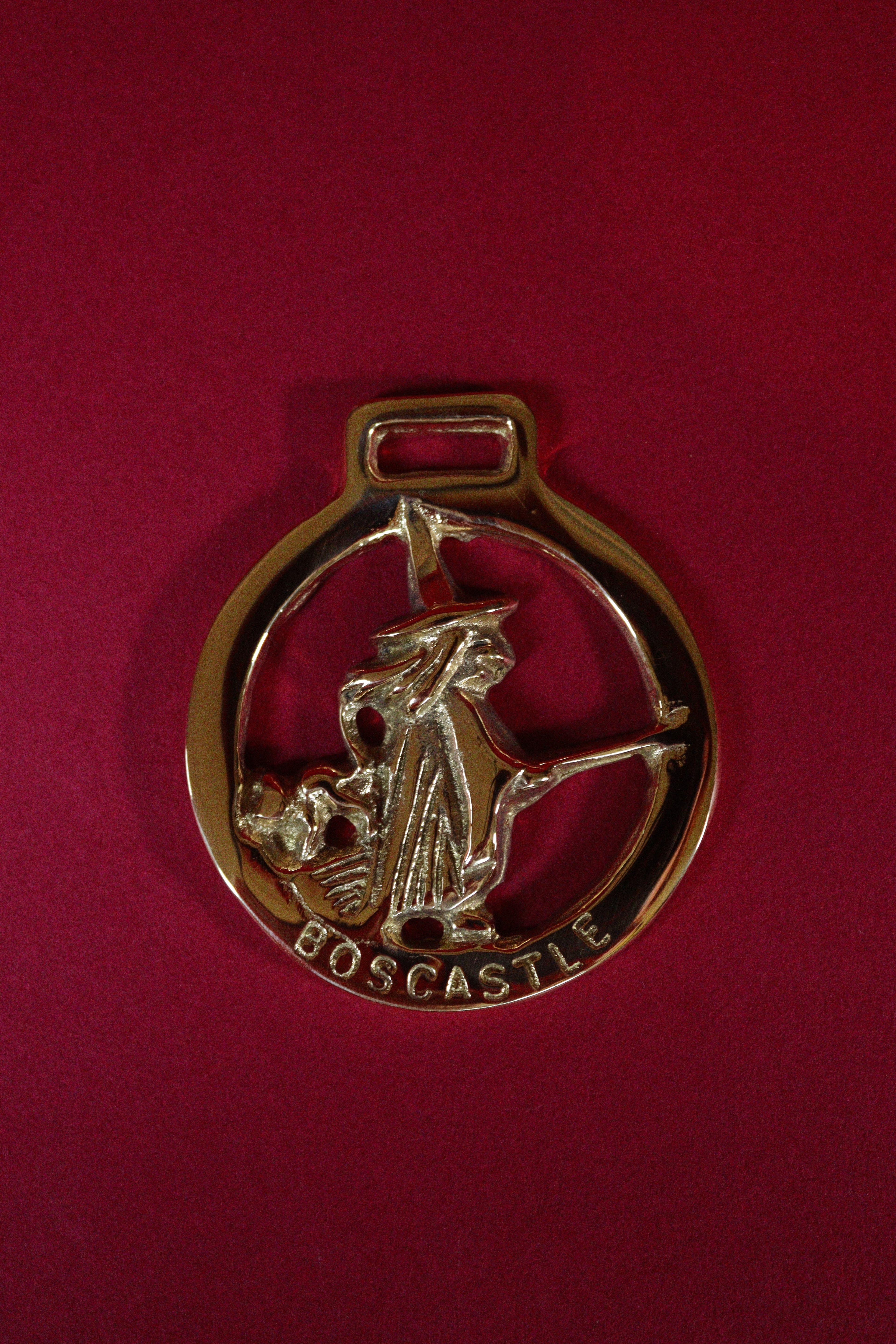 Brass pendant with a witch design on a red background