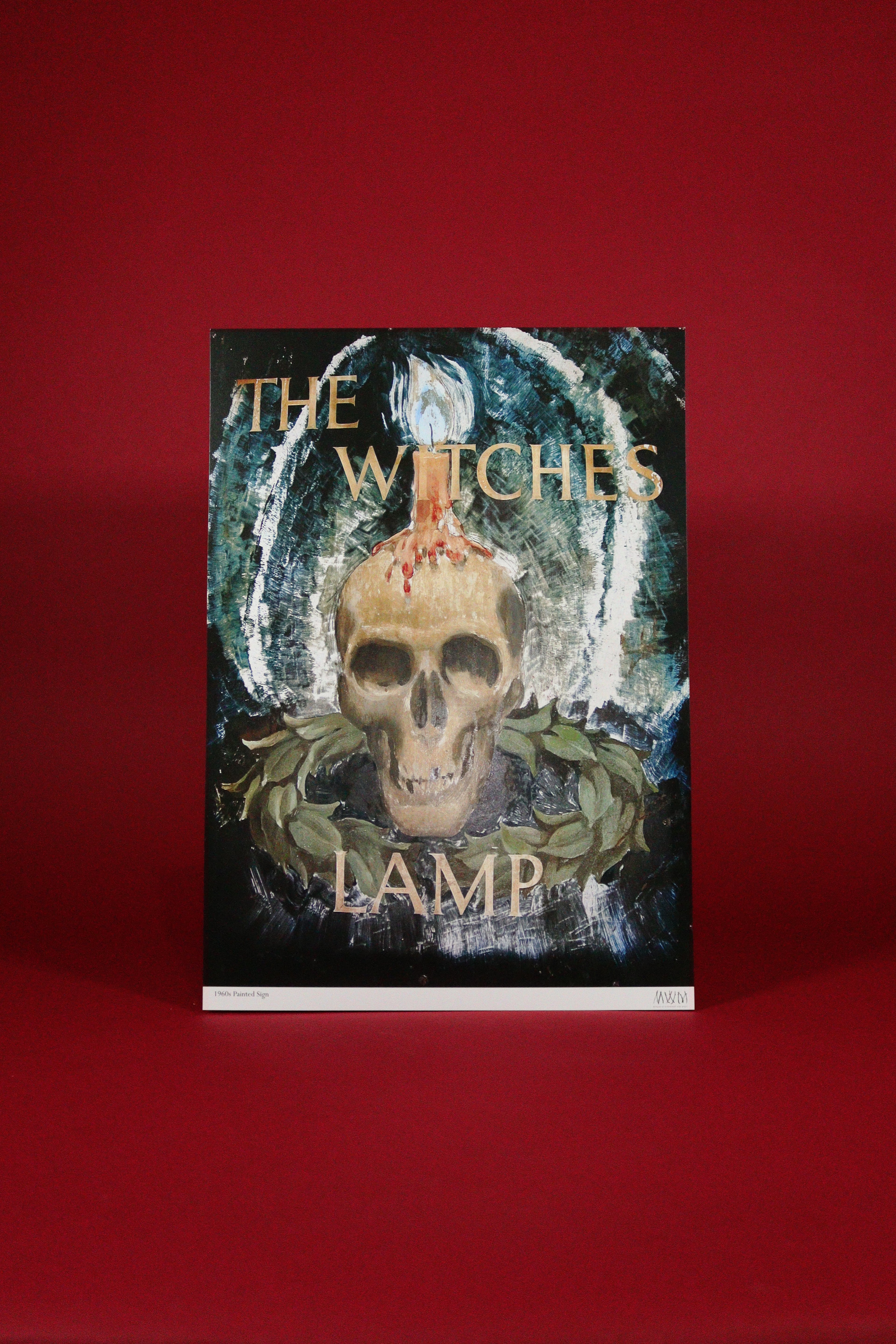 Poster with the words 'The Witches Lamp' with a skull and greenery design on a red background
