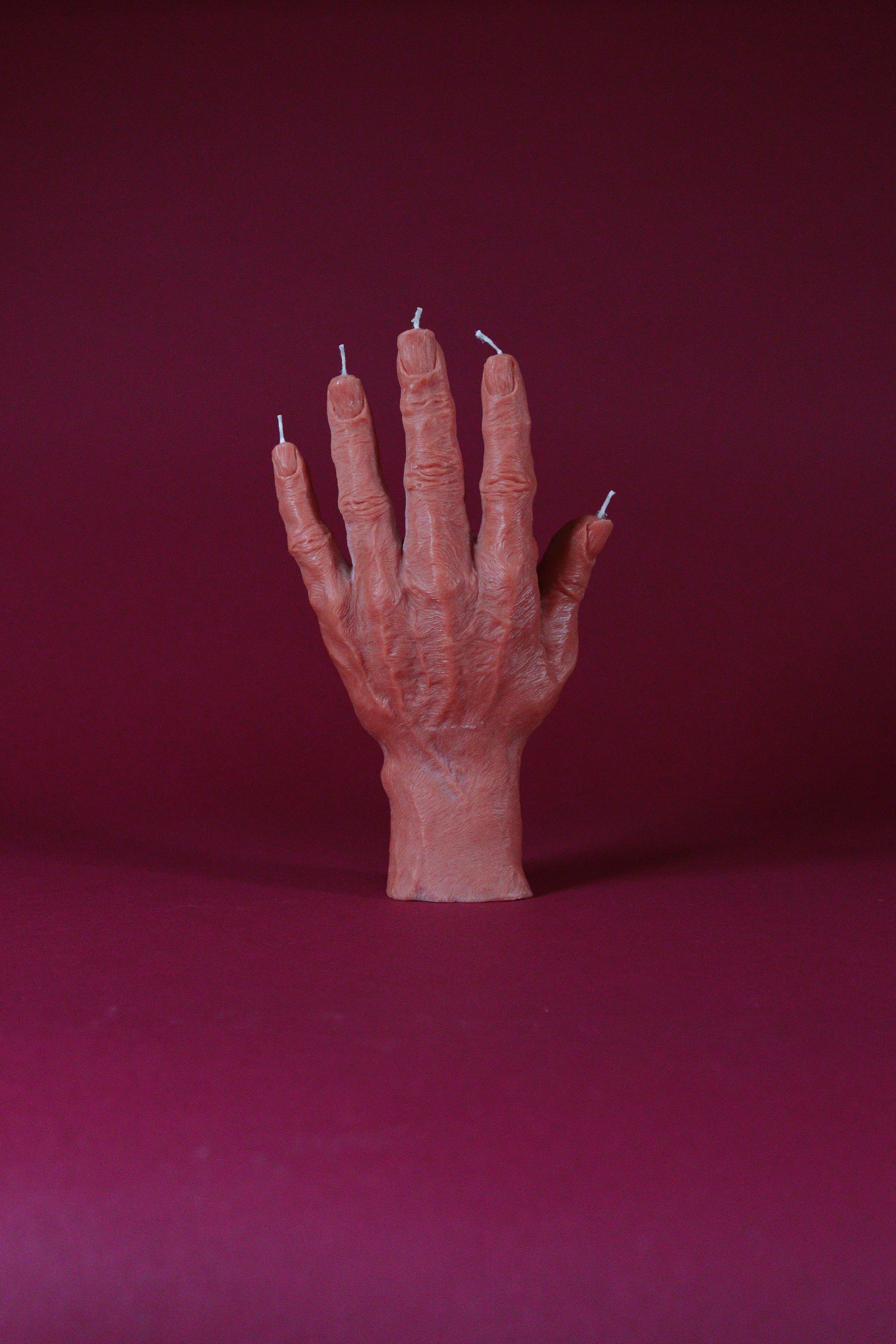 Candle shaped like a hand on a dark red background