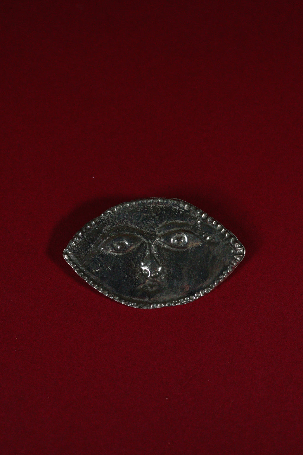 Decorative metal plate with face design on a red background