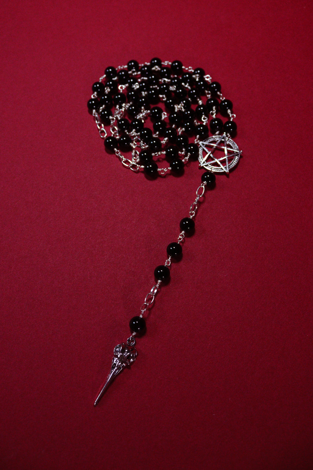 Black beaded necklace with silver pentagram and sword pendant on a red background