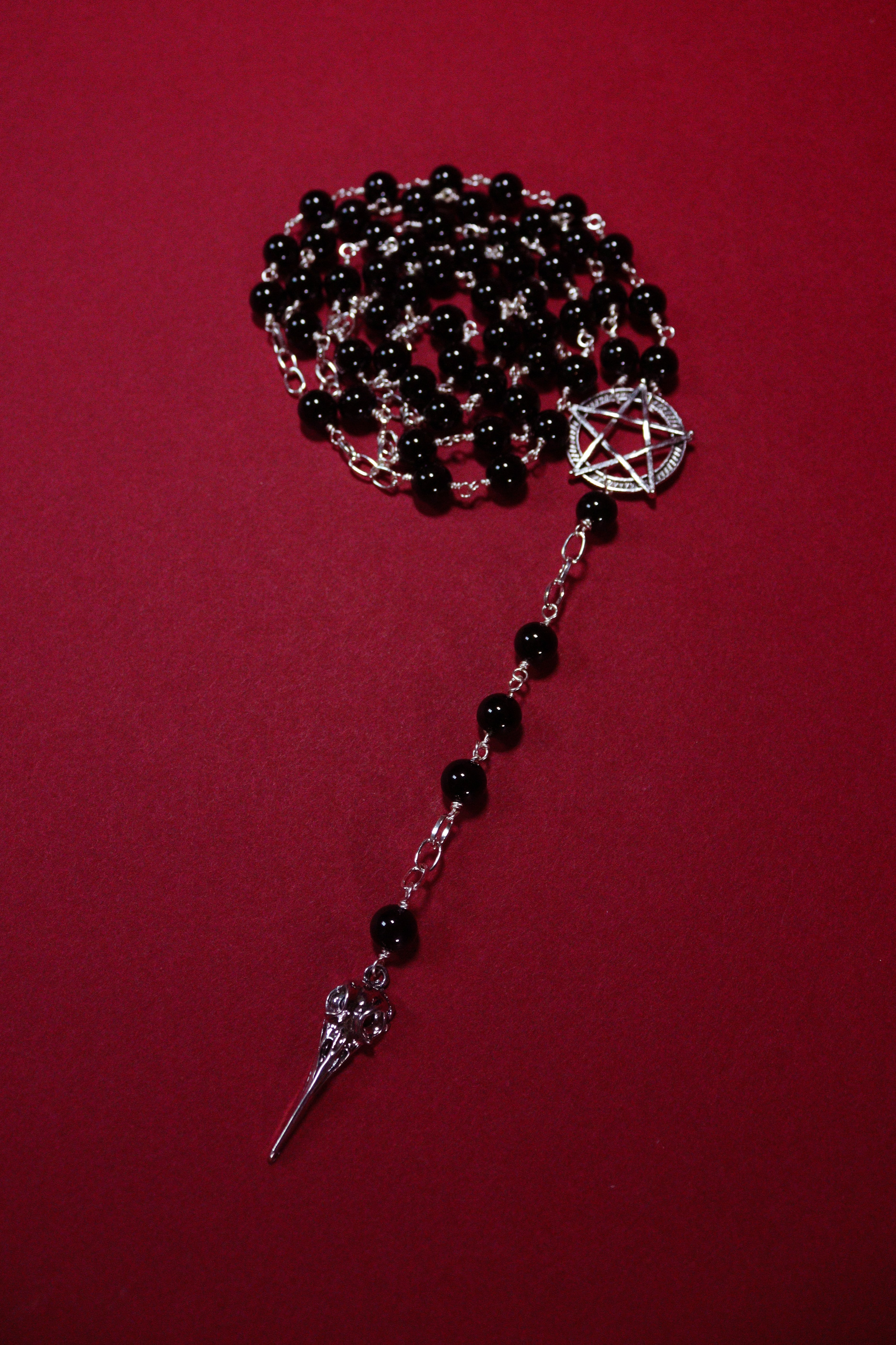 Black beaded necklace with silver pentagram and sword pendant on a red background