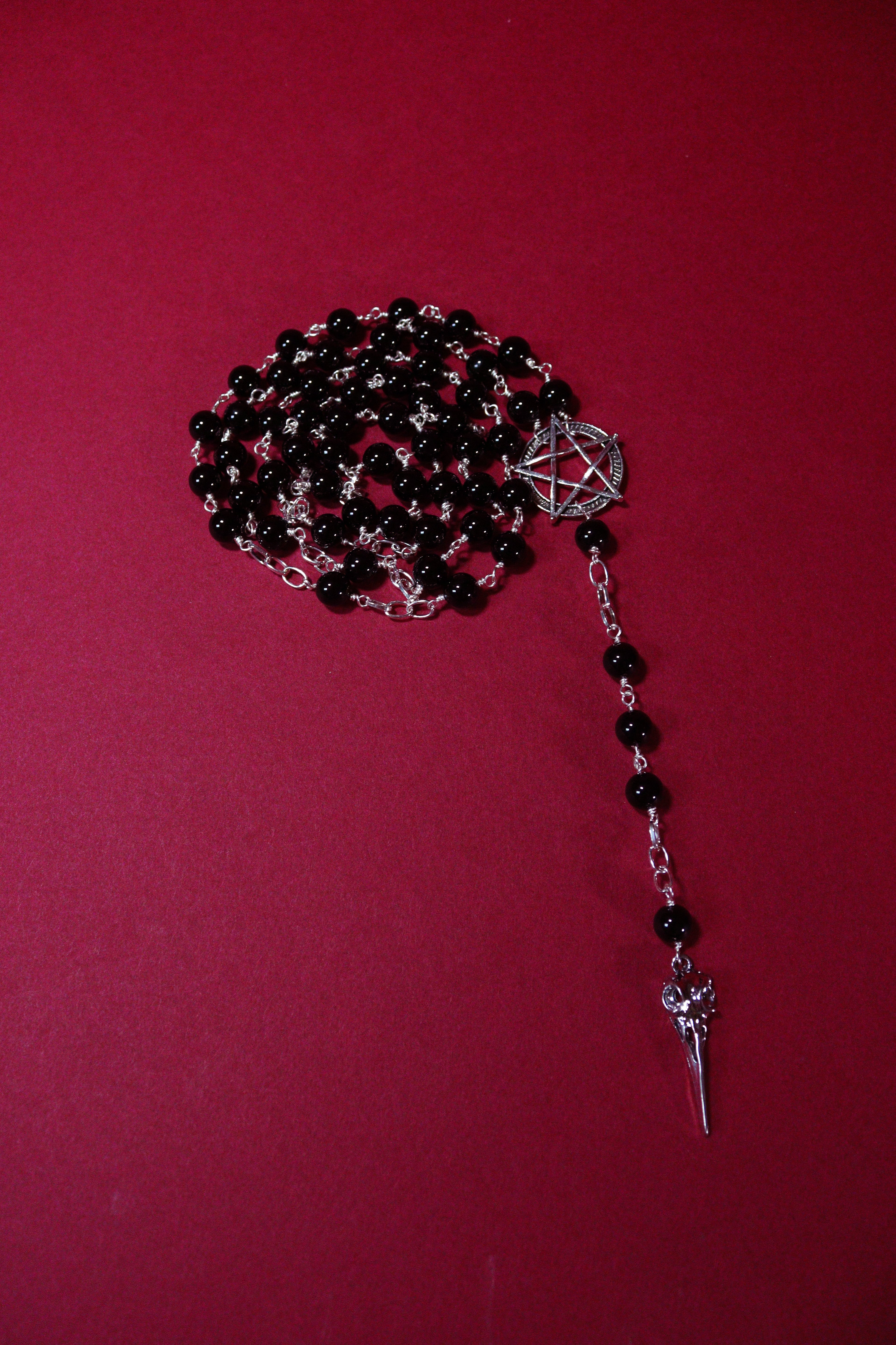 Black beaded rosary with silver cross on a red background