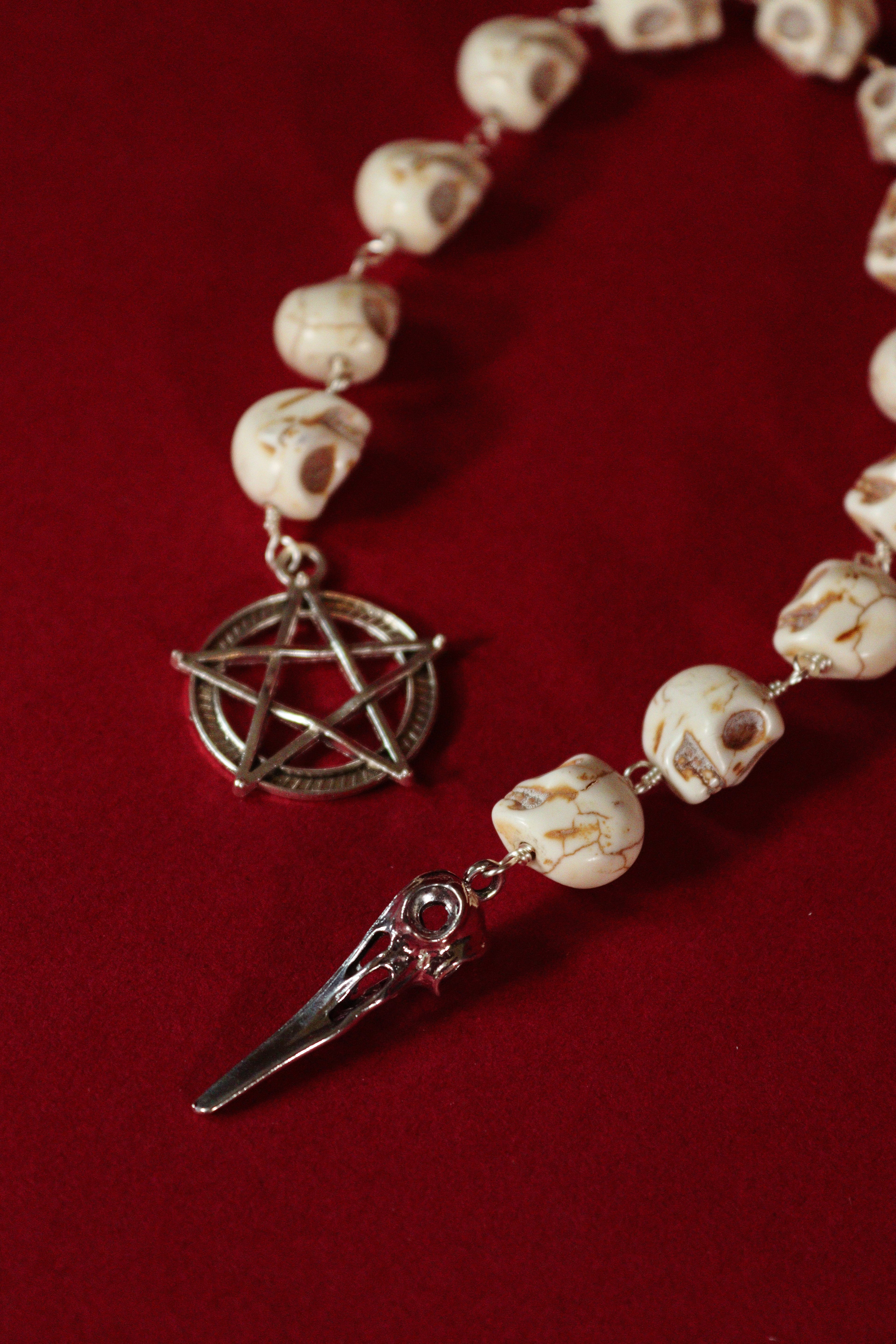 Necklace with skull beads and silver pentagram and dagger pendant on a red background