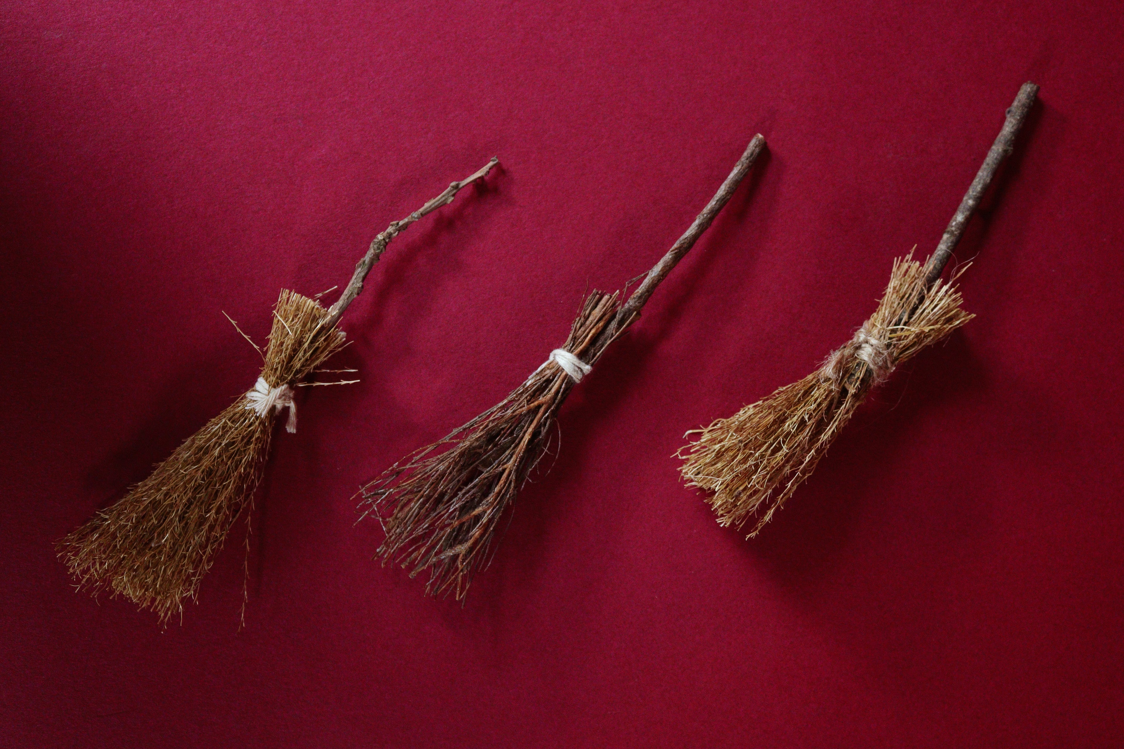 Three brooms of varying sizes on a red background