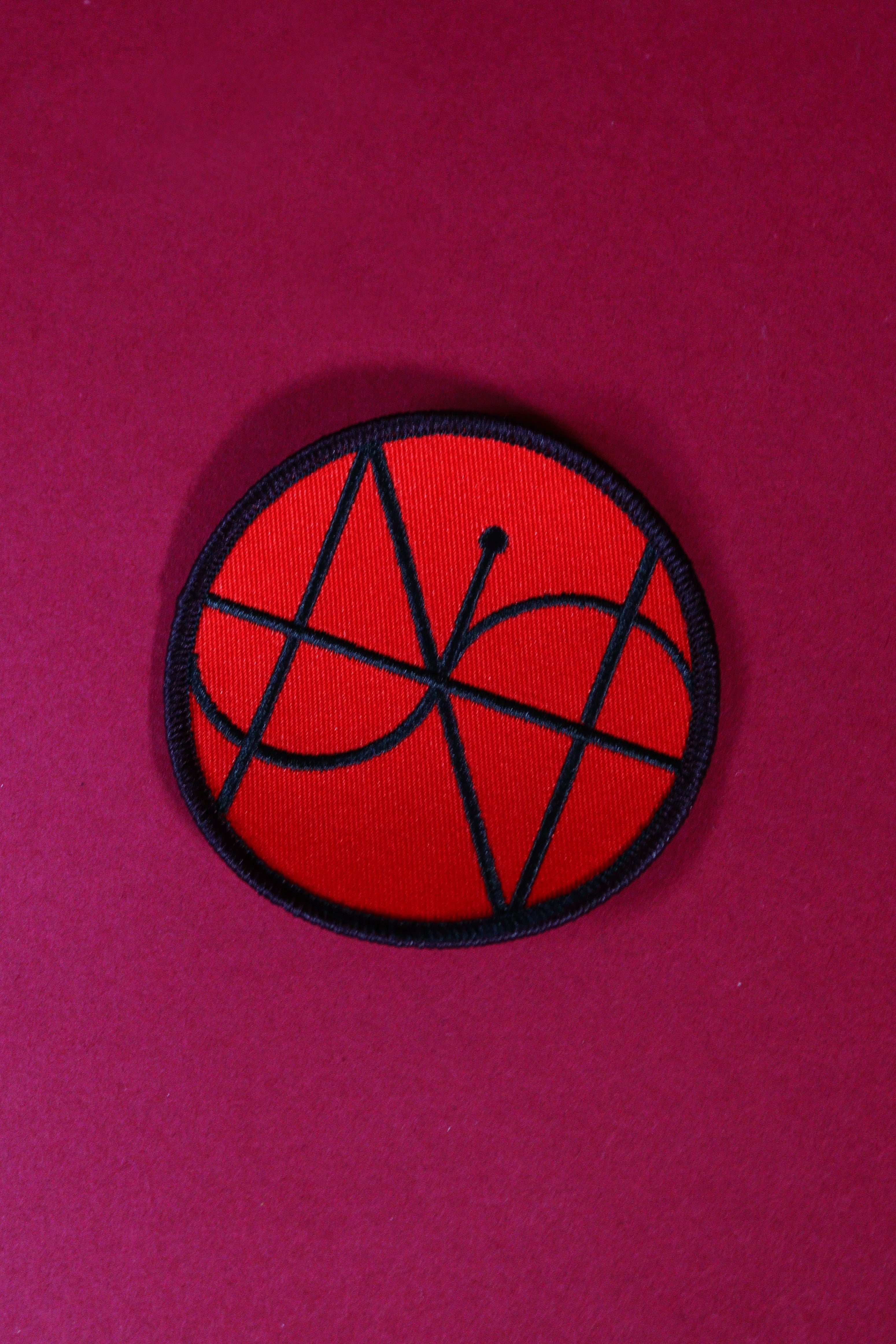 Red and black circular patch with geometric design on a pink background