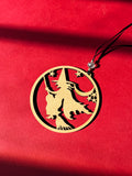 wood pendant with flying witch design on a red fabric background