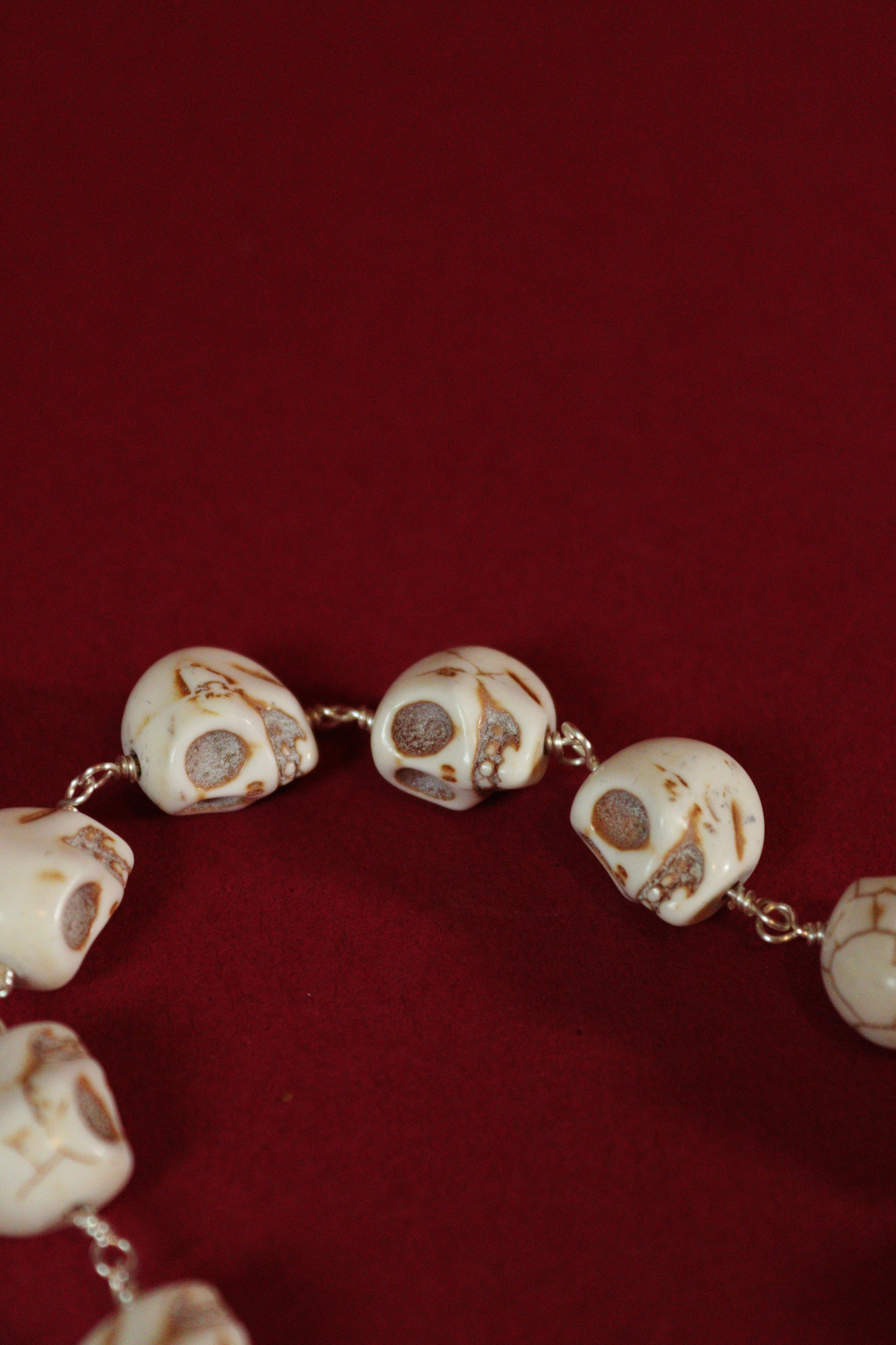 Close-up of a necklace with skull-shaped beads on a red background
